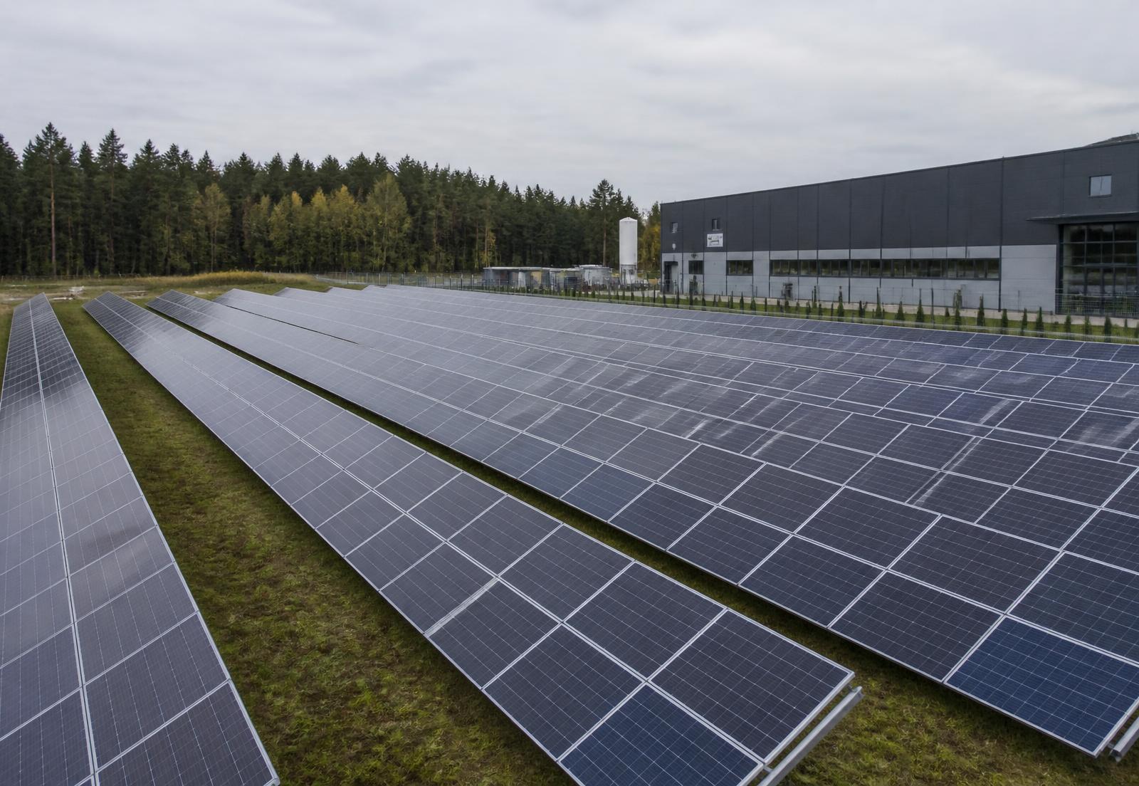 Solcellspark med rader av solpaneler intill en industrifastighet på Snebro Gård
